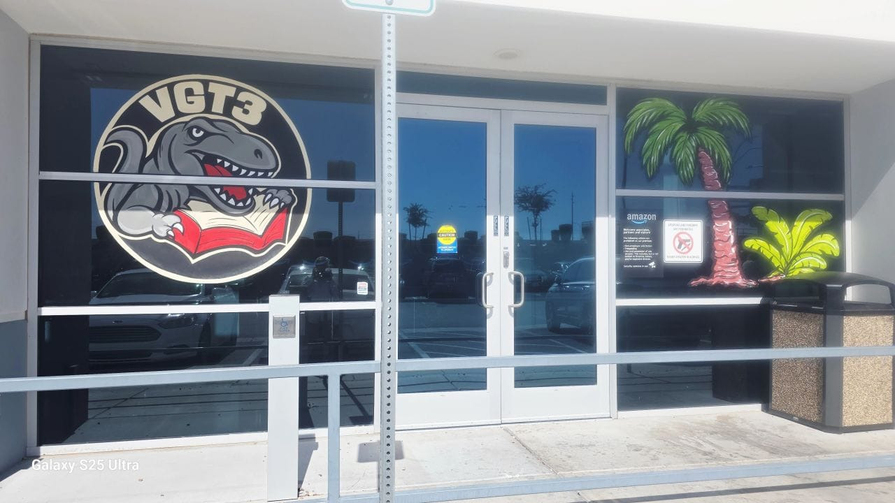 Photo of an office entrance. A logo in the window shows a red tyrannosaurus with a book, its claws clearly digging in and with a hint that it is more interested in destruction than reading.