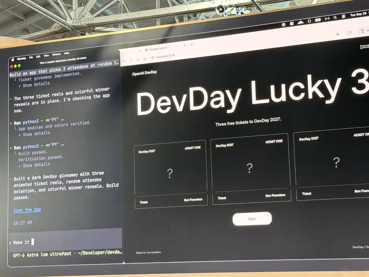 OpenAI DevDay 展区的一台大型显示器展示了一个深色的"DevDay Lucky 3"网页，提供三张 2027 年 DevDay 的免费门票，带有三张票卡和一个"旋转"按钮。旁边的编码助手面板显示赠品应用已构建完成，构建通过验证
